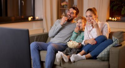 A happy family sit on a sofa eating popcorn and watching TV